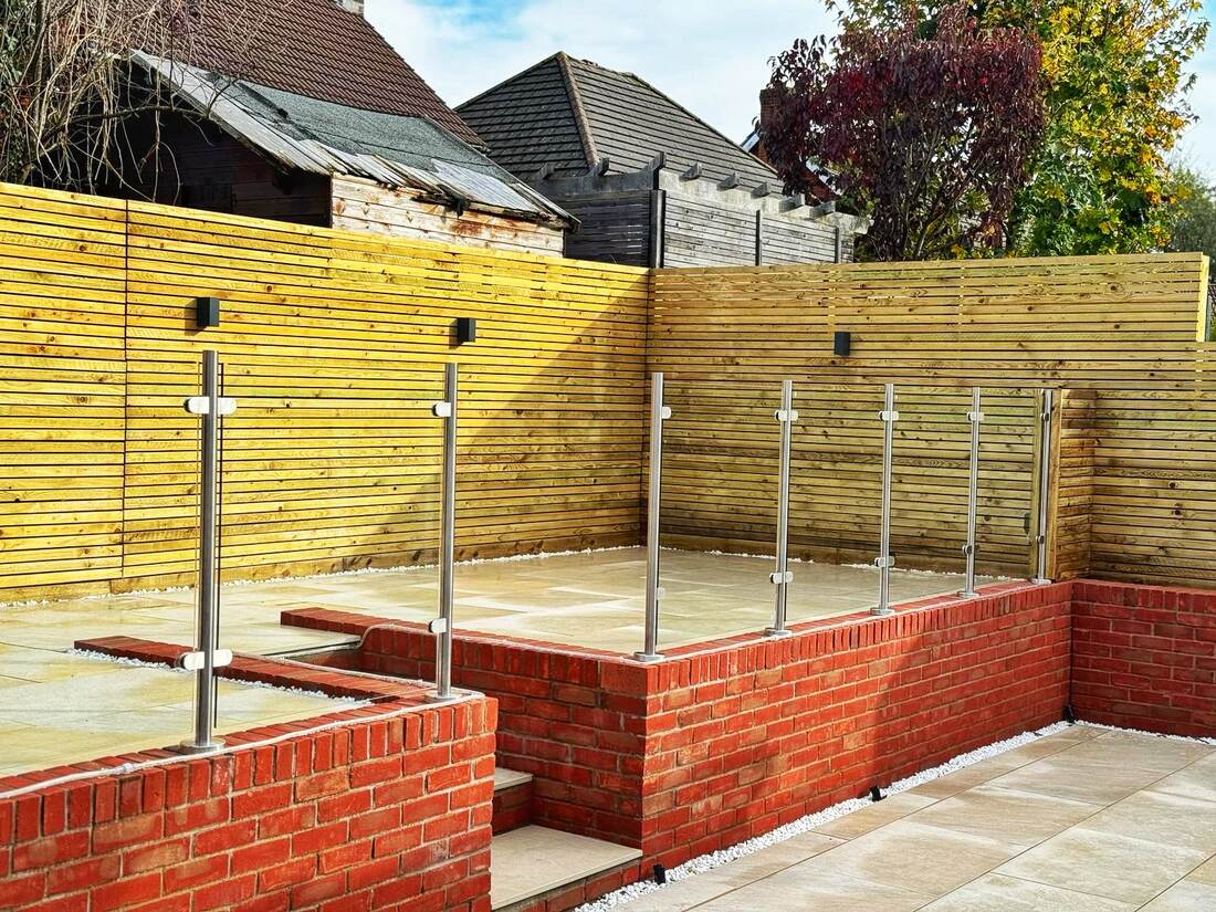 The same garden after landscaping, with sandstone paving, brick raised beds and a glass balustrade