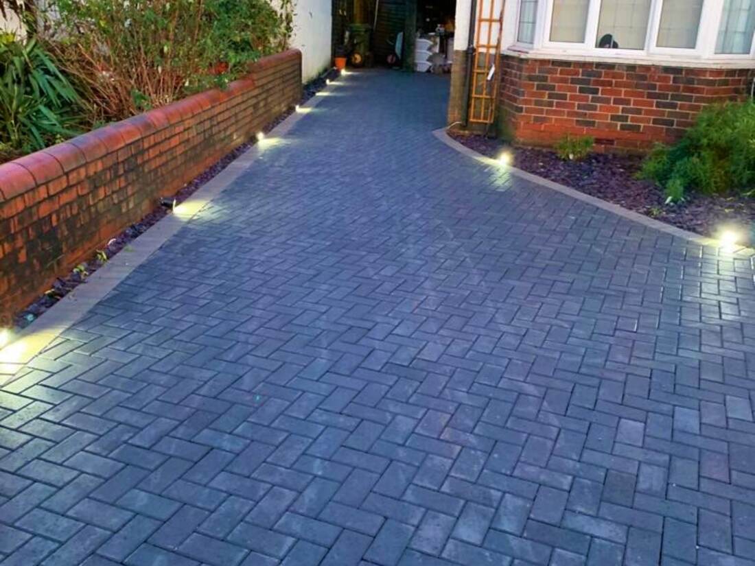 Dark herringbone block paved driveway lit at dusk