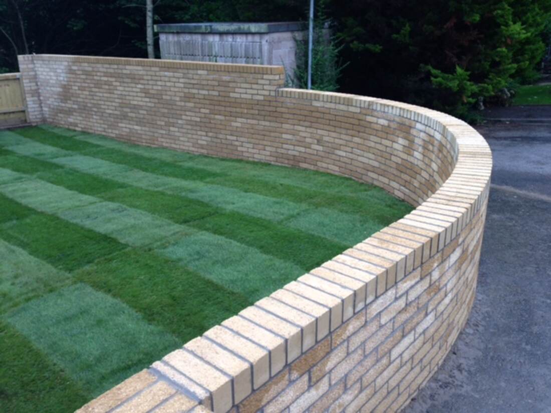 Curved cream brick retaining wall beside a striped lawn